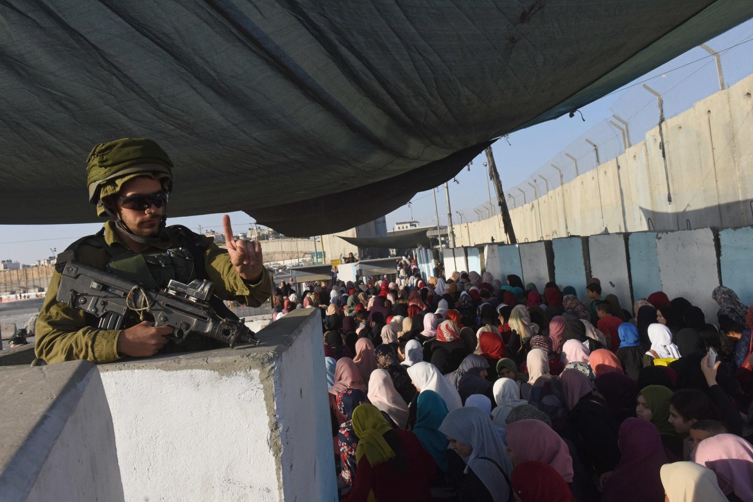 Israeli soldier motions to Palestinians queuing to cross Qalandiya checkpoint into Jerusalem to pray for Ramadan, 2018